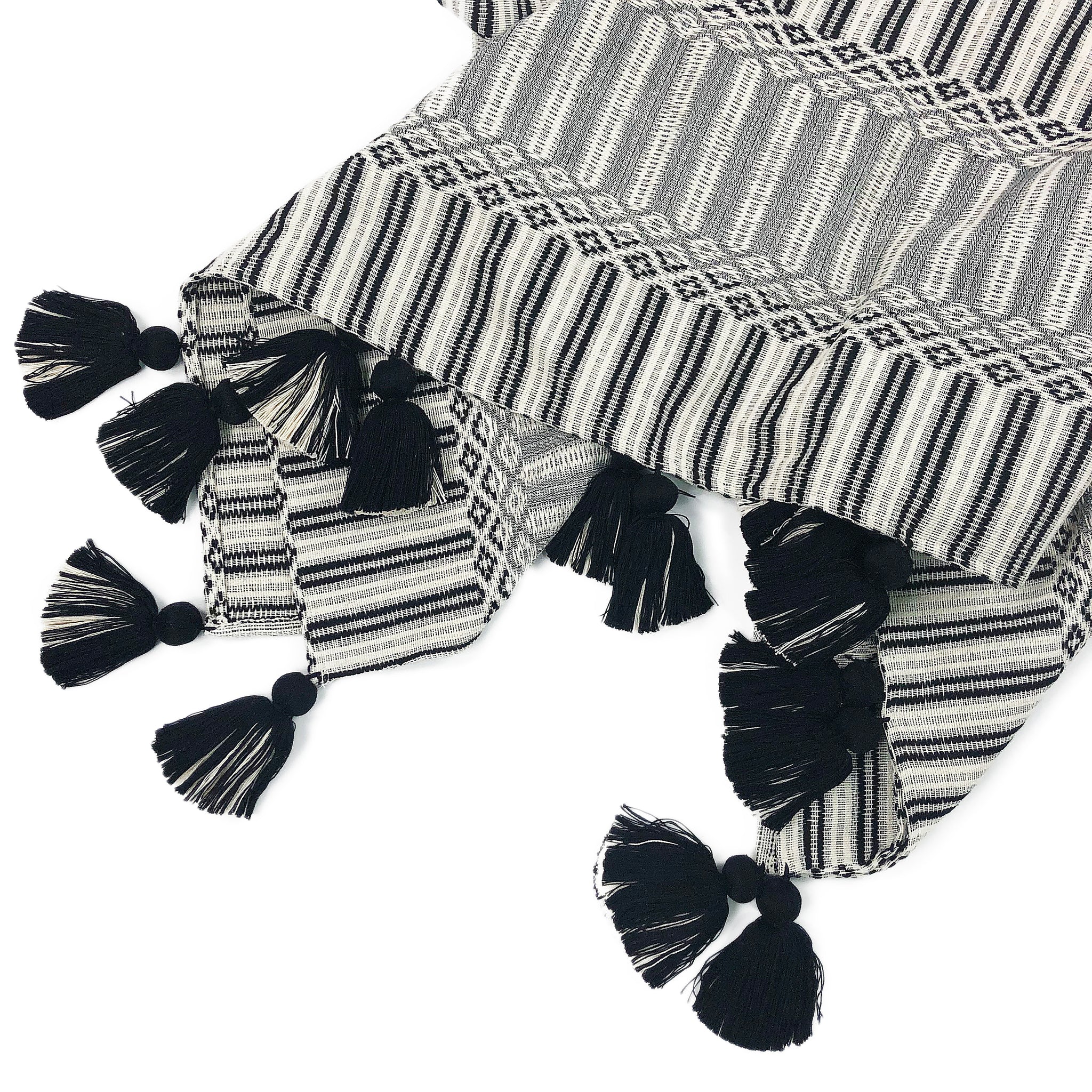 Volcanic Sands Throw by Del Palomar. Handmade in Guatemala. Handwoven authentic Guatemalan fabric throw, featuring an intricately woven textured pattern and adorned with black and white tassels. Handwoven on a traditional footloom by local artisans in Chimaltenango, Guatemala. Color black and white. 100% cotton.