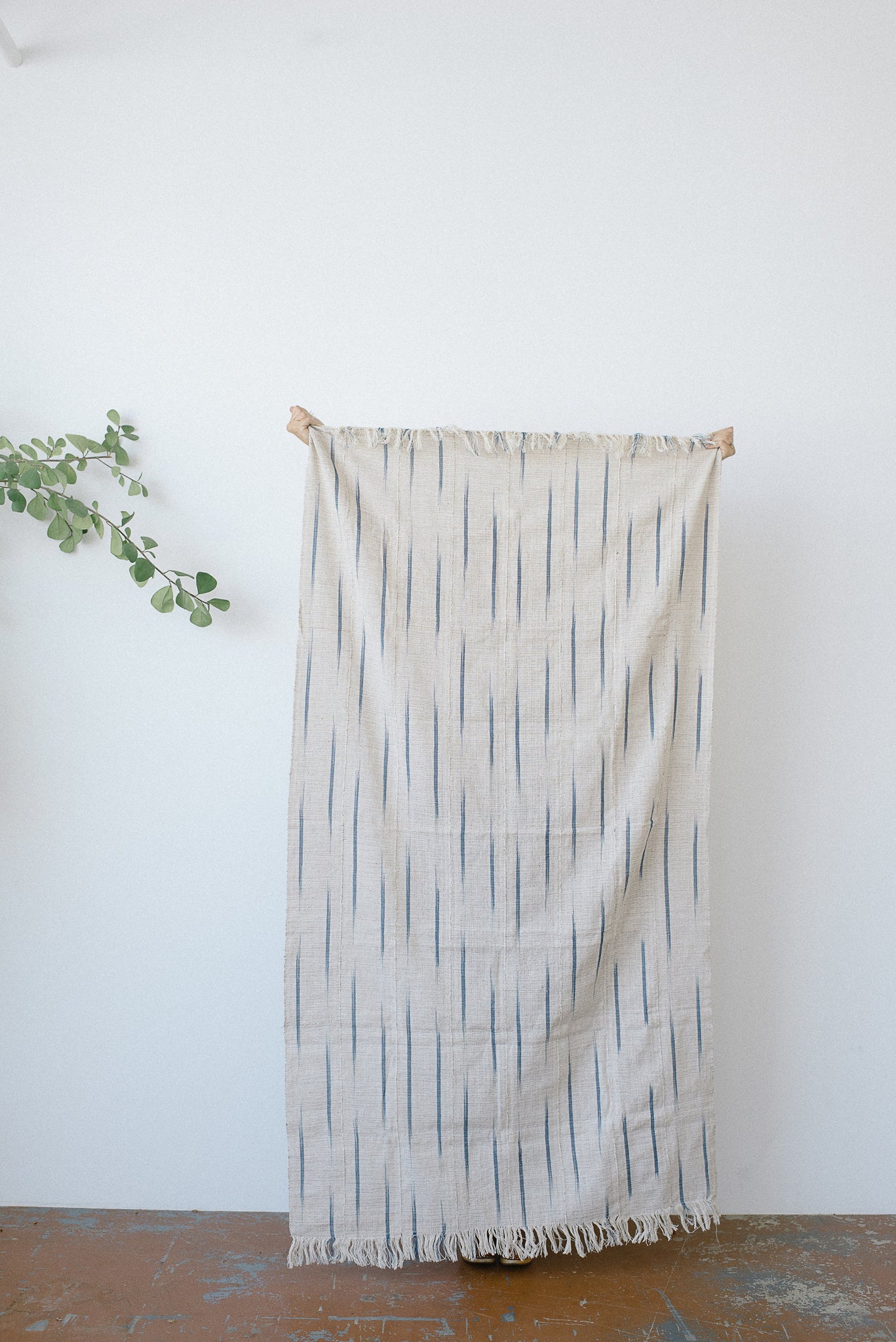Nori Siri Throw by Five Six Textiles. Handwoven in Côte d'Ivoire. A blend of white and brown threads interwoven with sparks of bright blue Siri Siri detail. Handwoven on handmade upright frame wooden looms using the same techniques that have been used for hundreds of years. Color natural blue. 100% raw cotton.